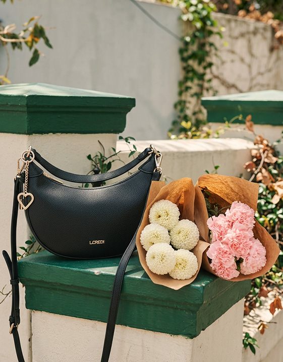 Dolce Vita - eine schwarze, elegante Handtasche und eine Tüte mit frischen Blumen liegen auf einer Mauer